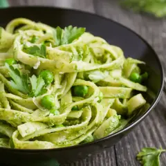 Pasta con espinacas y guisantes, cubierta con perejil fresco y queso rallado, servida en un tazón negro.