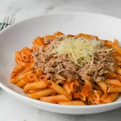 Macarrones con atún y queso rallado en un plato blanco, servidos con un tenedor y una servilleta a cuadros verdes.