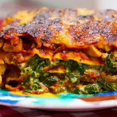 Porción de lasaña de verduras, con capas de pasta, espinacas y salsa de tomate, servida en un plato colorido.