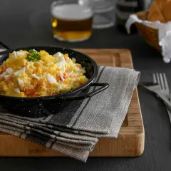Deliciosa ensaladilla rusa en un cuenco negro, con huevo duro picado y perejil. Acompañada de pan y cerveza.