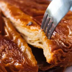 Un tenedor se hunde en un crujiente y caramelizado kouign amann, revelando sus capas hojaldradas.