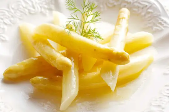 Delicados espárragos blancos, tiernos y jugosos, servidos en un plato blanco con un toque de eneldo.