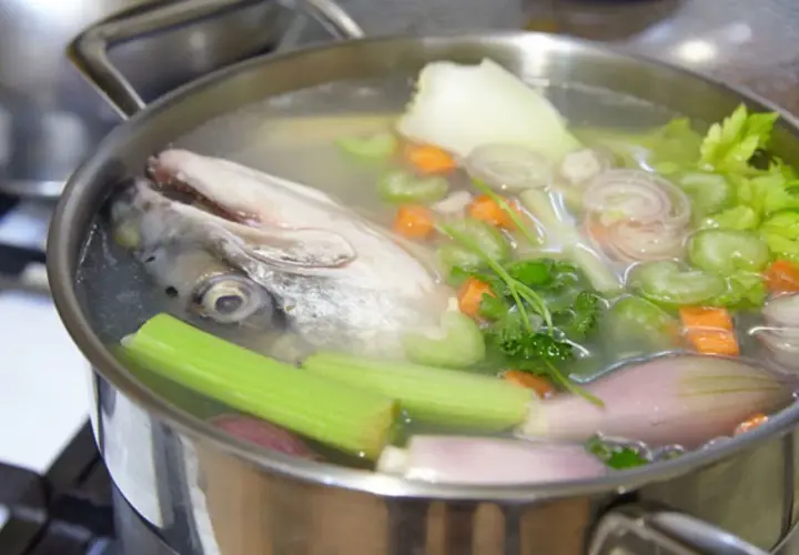Cabeza de pescado y verduras (zanahoria, apio, cebolla) hirviendo en una olla para hacer un rico caldo de pescado.