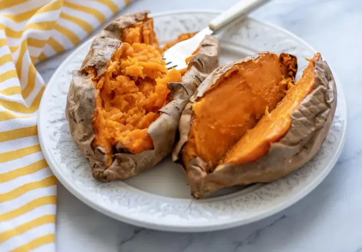 Dos mitades de boniato asado en freidora de aire, servidas en un plato blanco con un tenedor.