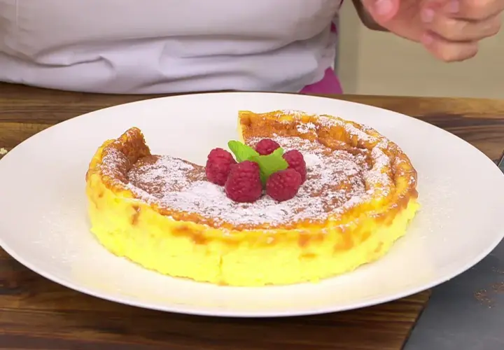 Tarta de queso Eva Arguiñano, dorada y esponjosa, espolvoreada con azúcar glas y decorada con frambuesas y menta.