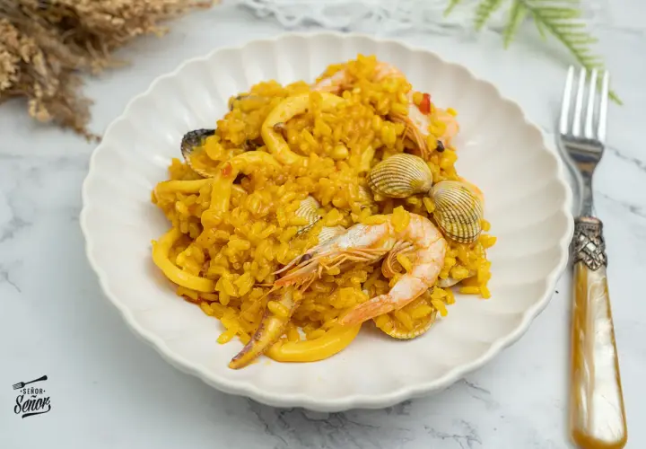 Deliciosa paella de marisco, con gambas, calamares y mejillones, servida en un plato blanco.