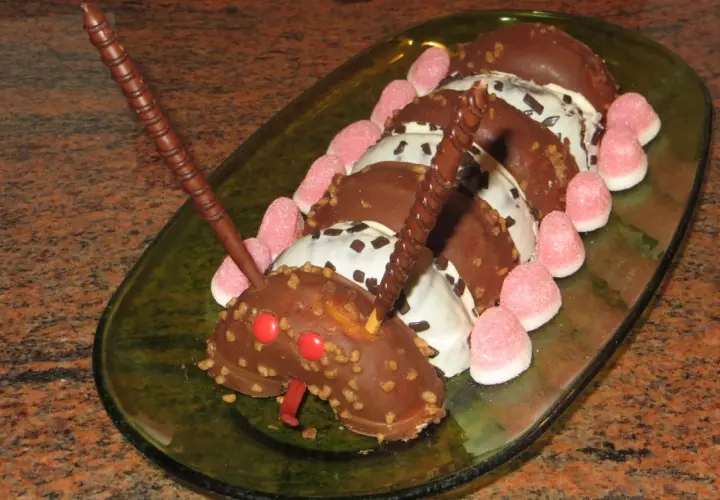 Tarta infantil con forma de oruga hecha de donuts cubiertos de chocolate, decorada con gominolas rosas y barquillos de chocolate.