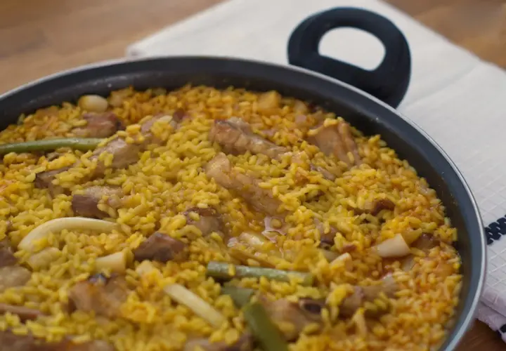Un delicioso arroz meloso con trozos de carne, judías verdes y calamar en una paellera.