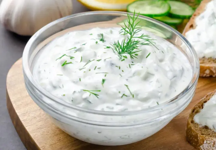 Un tazón de cremosa salsa de yogur con eneldo fresco, perfecto para untar en pan tostado.
