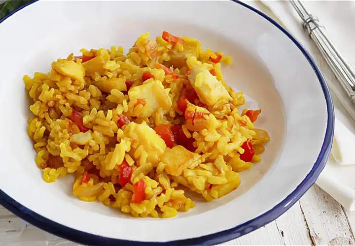 Un plato de arroz con bacalao, pimientos rojos y trozos de pescado blanco. Un delicioso arroz con bacalao listo para disfrutar.