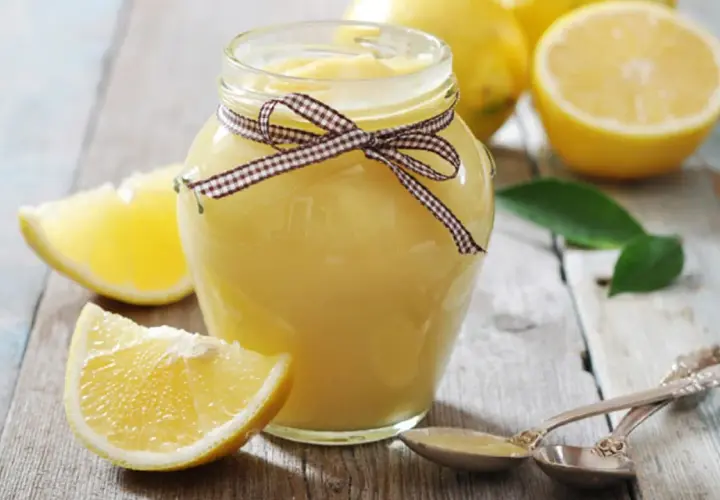 Tarro de lemon curd casero, decorado con un lazo, rodeado de limones frescos y rodajas.