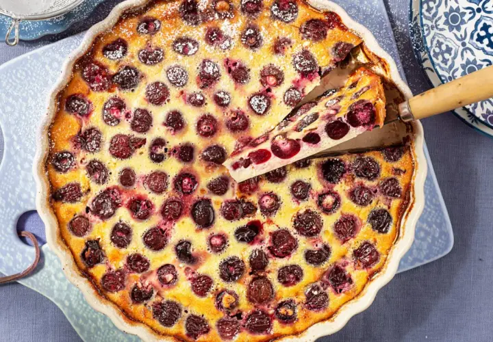 Un delicioso clafoutis de cerezas recién horneado, con una porción servida, espolvoreado con azúcar glas.