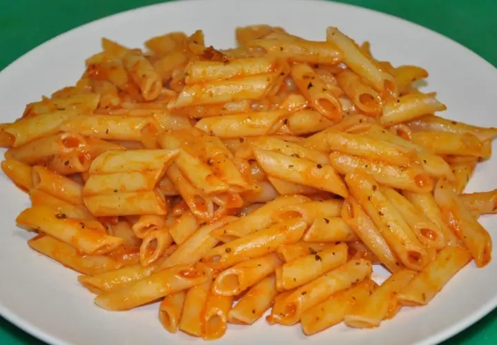 Un plato blanco lleno de macarrones con tomate, cubiertos con una salsa roja y especias.
