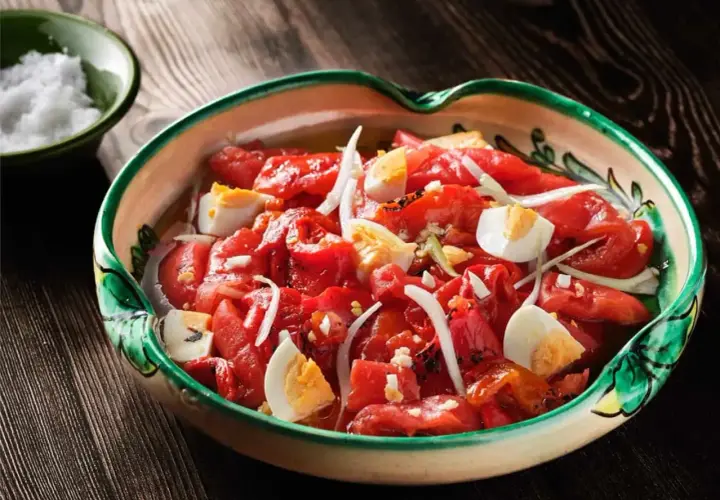 Zorongollo extremeño, una ensalada de pimientos asados, cebolla y huevo duro, servida en una cazuela de barro decorada.