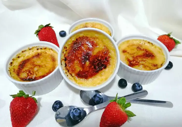 Cuatro cremosos creme brulee con una capa caramelizada, adornados con fresas y arándanos frescos.