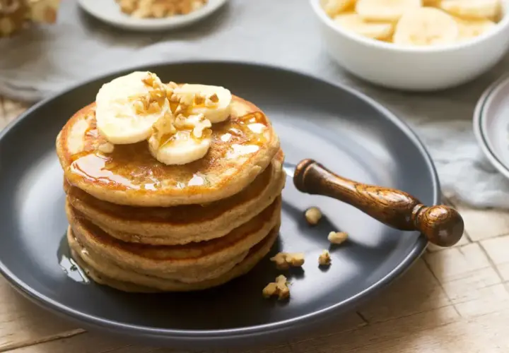 Pila de tortitas esponjosas cubiertas con plátano, nueces y sirope. ¡Una deliciosa receta de tortitas para el desayuno!