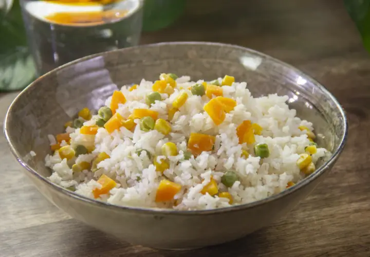 Un tazón de arroz blanco con trozos de zanahoria, guisantes y maíz. Un plato sencillo y colorido de arroz con verduras.