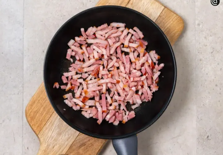 Trozos de bacon crudo en una sartén negra sobre una tabla de madera. Preparando la base para una deliciosa mermelada de bacon.