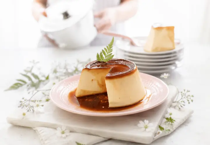 Delicioso flan de queso con caramelo líquido, decorado con una hoja verde y flores delicadas.