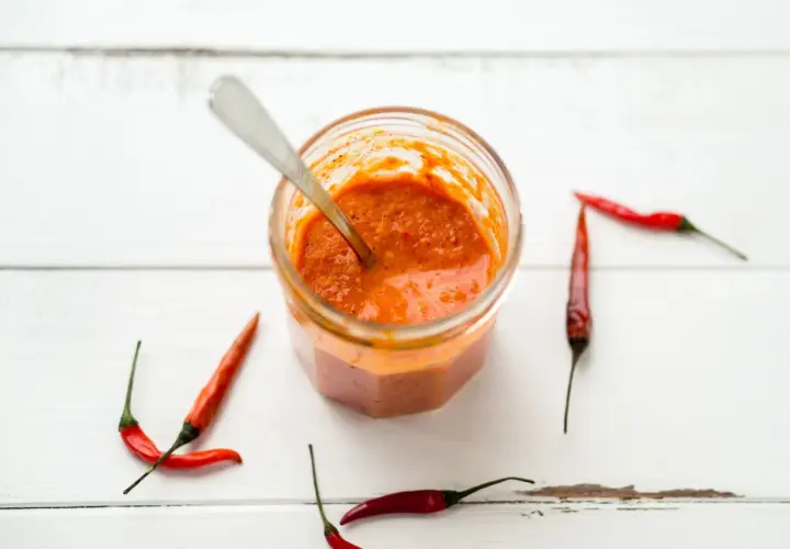 Tarro de cristal con salsa piri piri y chiles rojos alrededor, listo para dar un toque picante a tus platos.