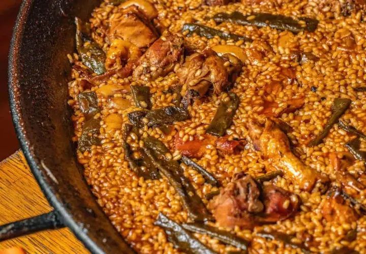 Paella de pollo y judías verdes, con el arroz ligeramente quemado en el fondo, creando un socarrat crujiente.