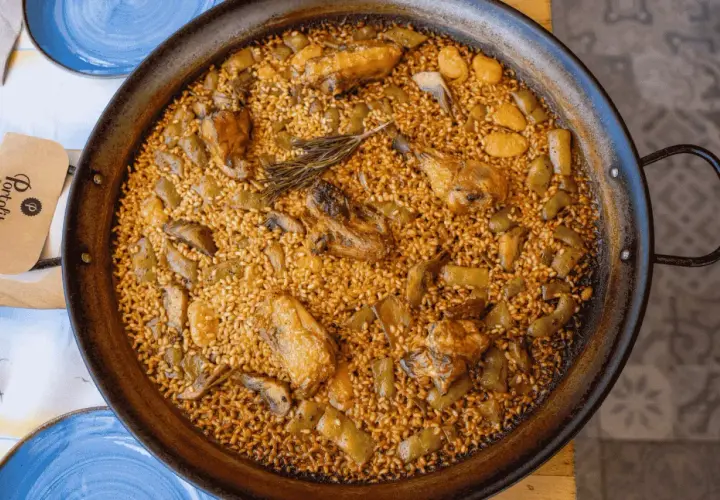 Paella valenciana que lleva pollo, conejo y verduras, con un toque de romero. Un plato tradicional y delicioso.
