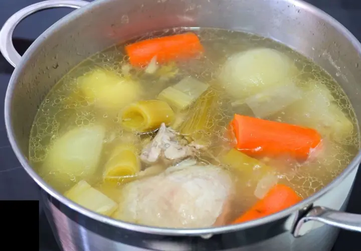 Olla con caldo de pollo casero burbujeante, con trozos de zanahoria, puerro y patata.