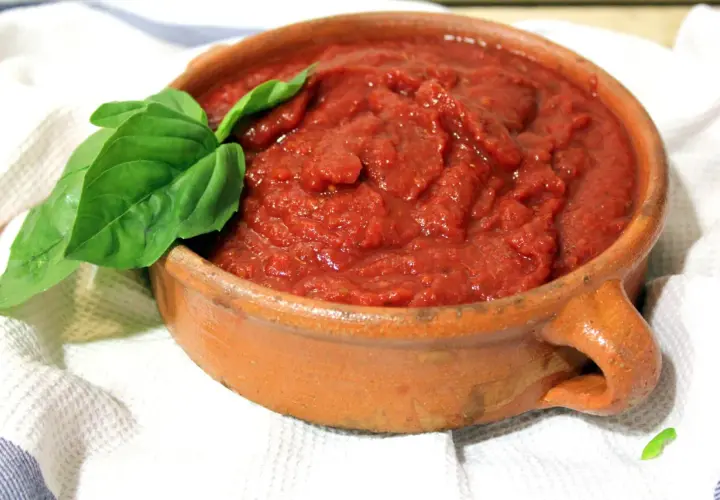 Salsa napolitana casera en cazuela de barro, decorada con hojas de albahaca fresca.