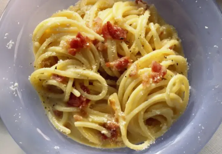 Un plato de pasta carbonara cremoso, con trozos de panceta crujiente y espolvoreado con queso rallado.