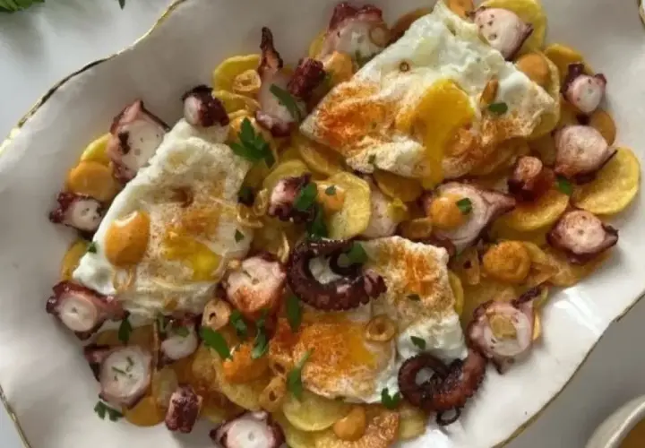 Delicioso plato de pulpo con patatas y huevos rotos, espolvoreado con pimentón y perejil.