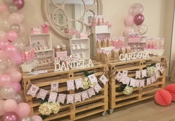 Mesa dulce para comunión de niña, con candy bar casero, globos rosas y blancos, y detalles personalizados.