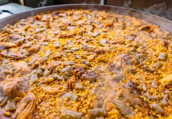 Paella humeante con pollo, judías verdes y trozos de carne. El arroz bomba es el que mejor absorbe el sabor, ideal para esta paella.