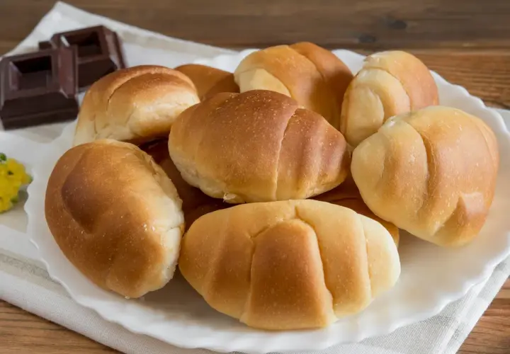 Un plato blanco con pan de leche dorado y suave, junto a trozos de chocolate oscuro.