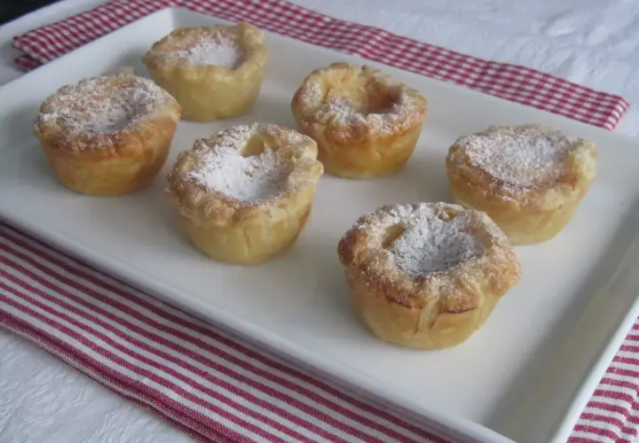 Seis pastelitos de arroz dorados, espolvoreados con azúcar glas, en una bandeja blanca.