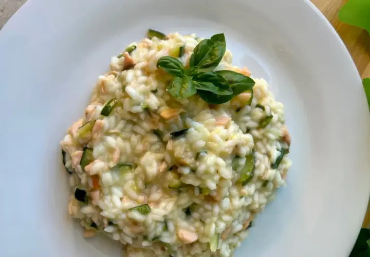 Cremoso arroz a la milanesa con salmón y calabacín, adornado con hojas de albahaca fresca.
