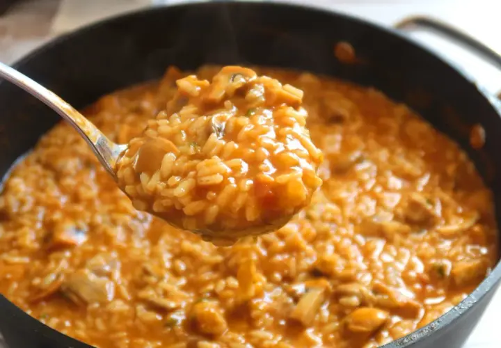 Cuchara sirviendo un delicioso arroz caldoso con pollo y trozos de champiñones.