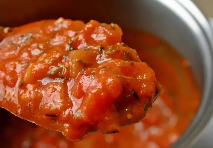 Cuchara llena de sabrosa salsa de tomate casera, con trozos de tomate y hierbas.