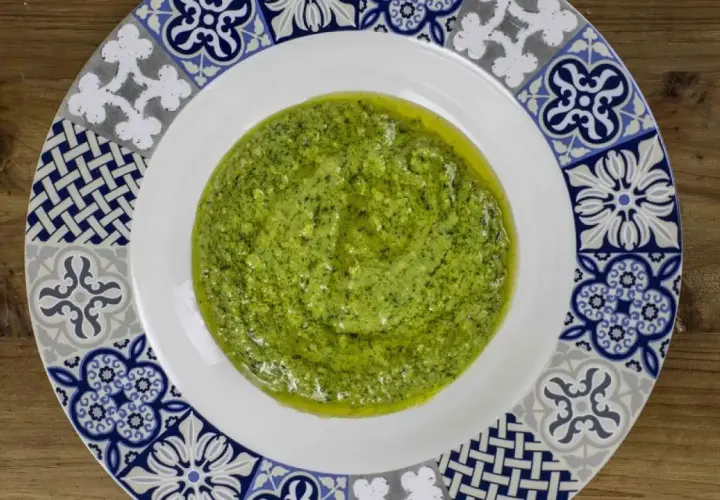 Un plato blanco con un borde decorado con azulejos presenta una generosa porción de vibrante salsa pesto, lista para realzar cualquier plato.