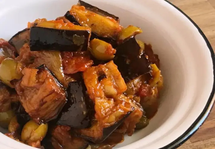 Un plato de caponata siciliana, con berenjenas, aceitunas y tomate, servido en un cuenco blanco.
