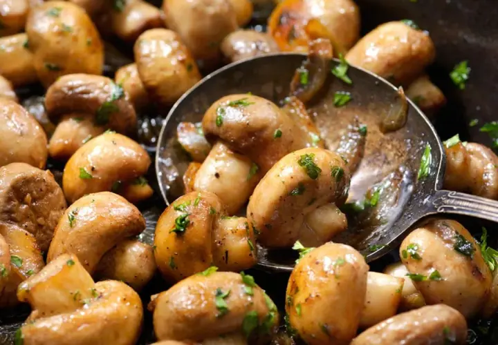 Champiñones salteados con perejil, perfectos para tus recetas con champiñones. Una cuchara sirve para cogerlos.