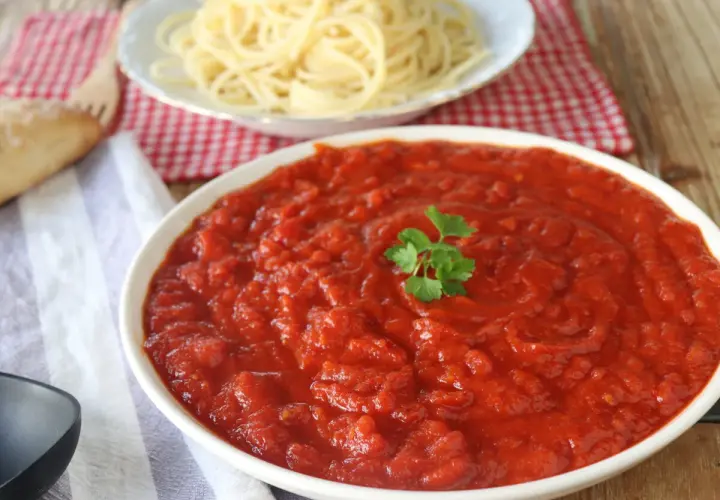 Un tazón de vibrante salsa arrabiata, decorado con perejil, junto a espaguetis y pan.