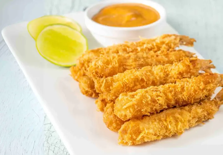 Crujientes gambas a la gabardina doradas, servidas con rodajas de lima y una salsa cremosa.