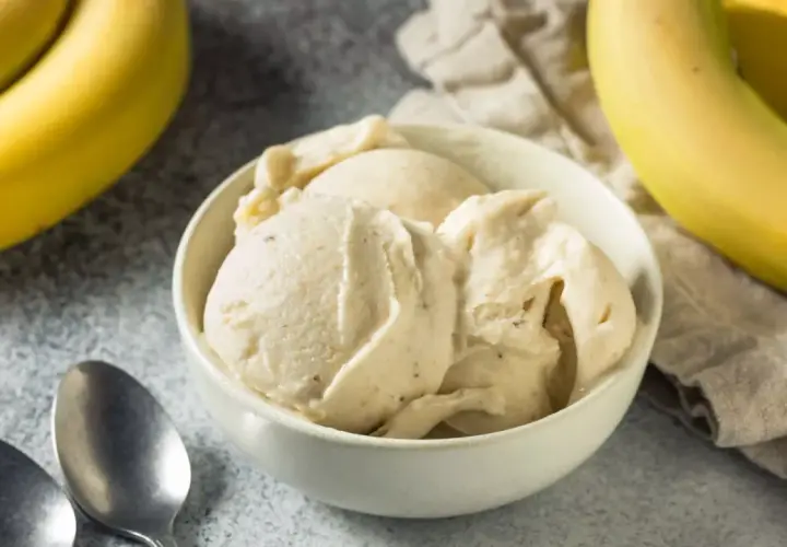 Un cremoso helado de plátano en un tazón blanco, con plátanos amarillos frescos al lado.