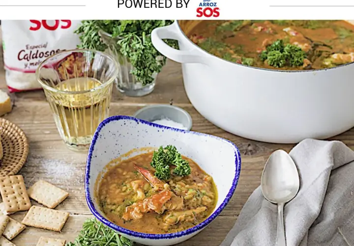 Delicioso arroz con bogavante servido en un cuenco, con una cazuela llena al fondo. Galletas y hierbas frescas acompañan este plato.