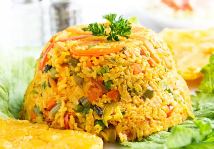 Un montículo de arroz con pollo, adornado con perejil, servido sobre hojas de lechuga y acompañado de plátanos fritos.