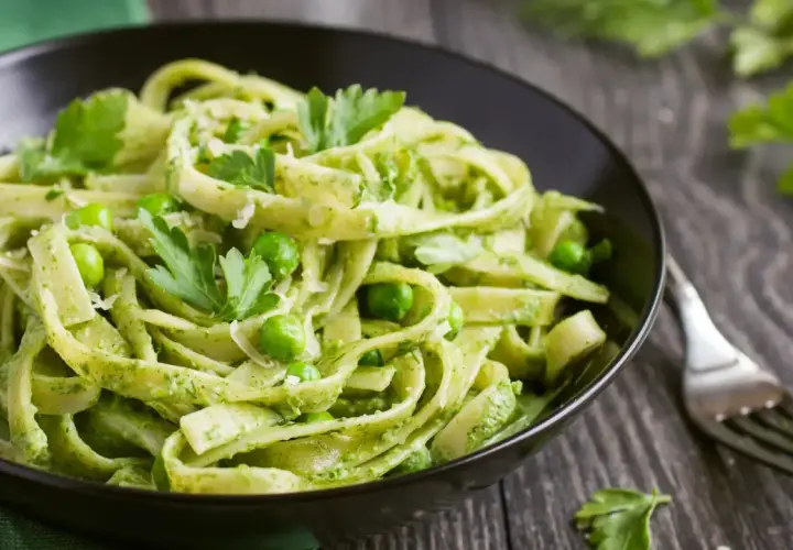 Pasta con espinacas y guisantes, cubierta con perejil fresco y queso rallado, servida en un tazón negro.