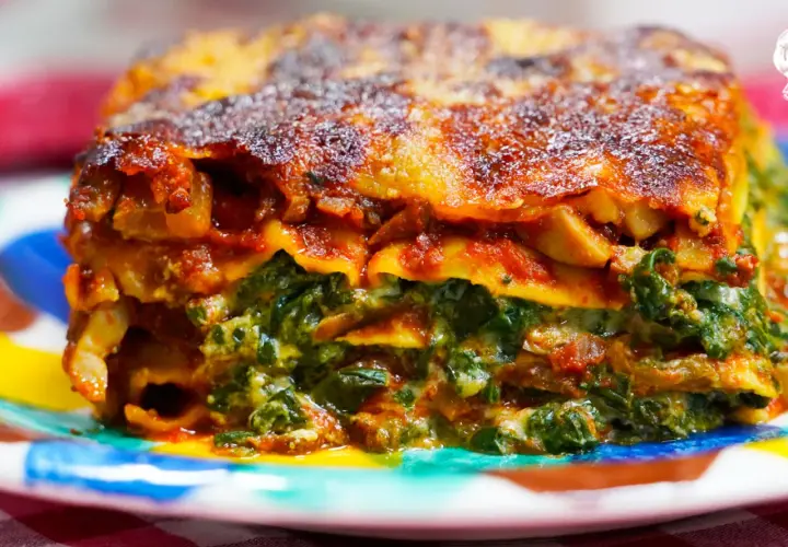 Porción de lasaña de verduras, con capas de pasta, espinacas y salsa de tomate, servida en un plato colorido.