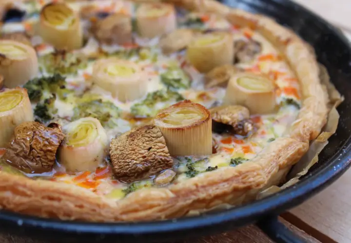 Quiche de verduras recién horneada, con puerros, brócoli y champiñones, lista para disfrutar.