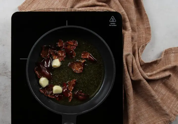 Sartén con aceite, ajos y trozos de pimiento rojo, preparando la base para una salmorreta receta.