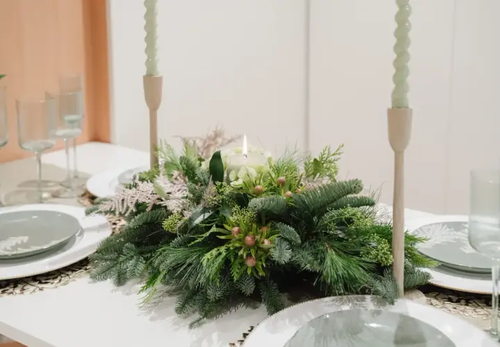 Centros de mesa de navidad sencillas con velas y follaje verde. Copas y platos listos para una cena festiva.